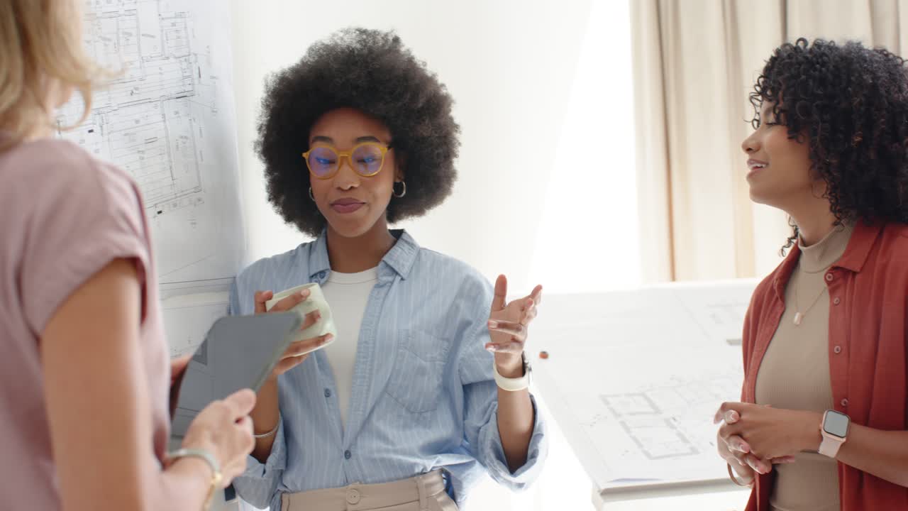 Diverse women in studio viewing tablet lead woman adjusting yellow glasses with mug, checking plans