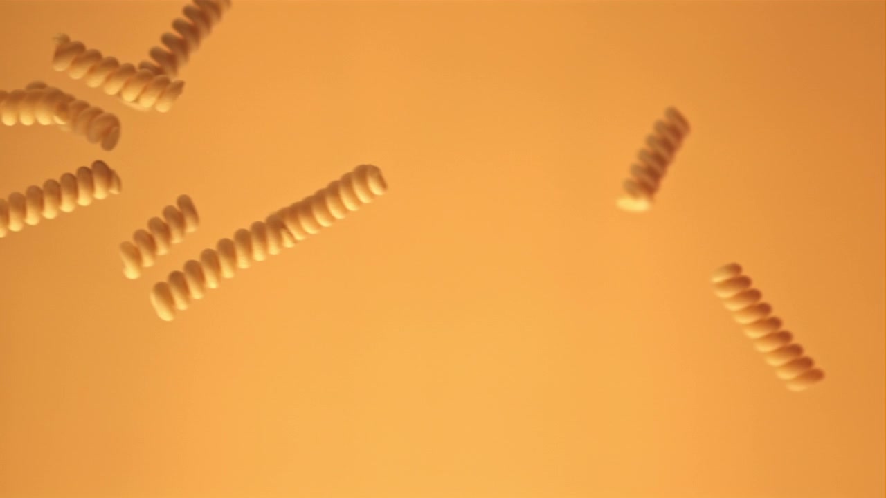 Uncooked Fusilli Pasta Falling in Slow Motion Against an Orange Background