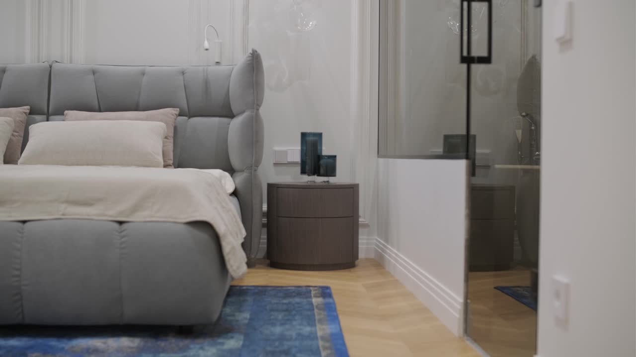 un lujoso dormitorio con un elegante cabecera de mechón y una llamativa alfombra azul se convierte sin problemas en un elegante baño con accesorios modernos y un espejo oval único, capturando un diseño que fusiona la comodidad con la elegancia.