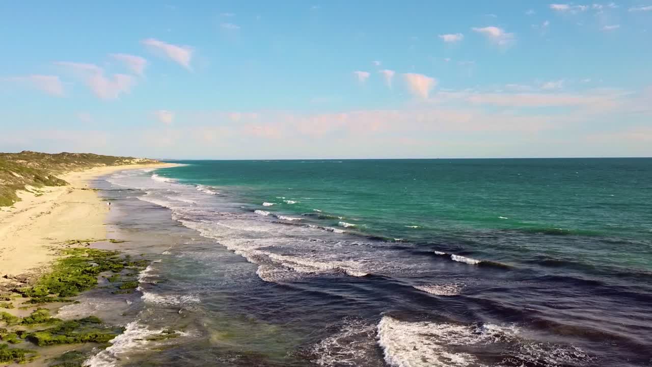 Waves gently roll onto a scenic shoreline on a bright sunny day with clear skies