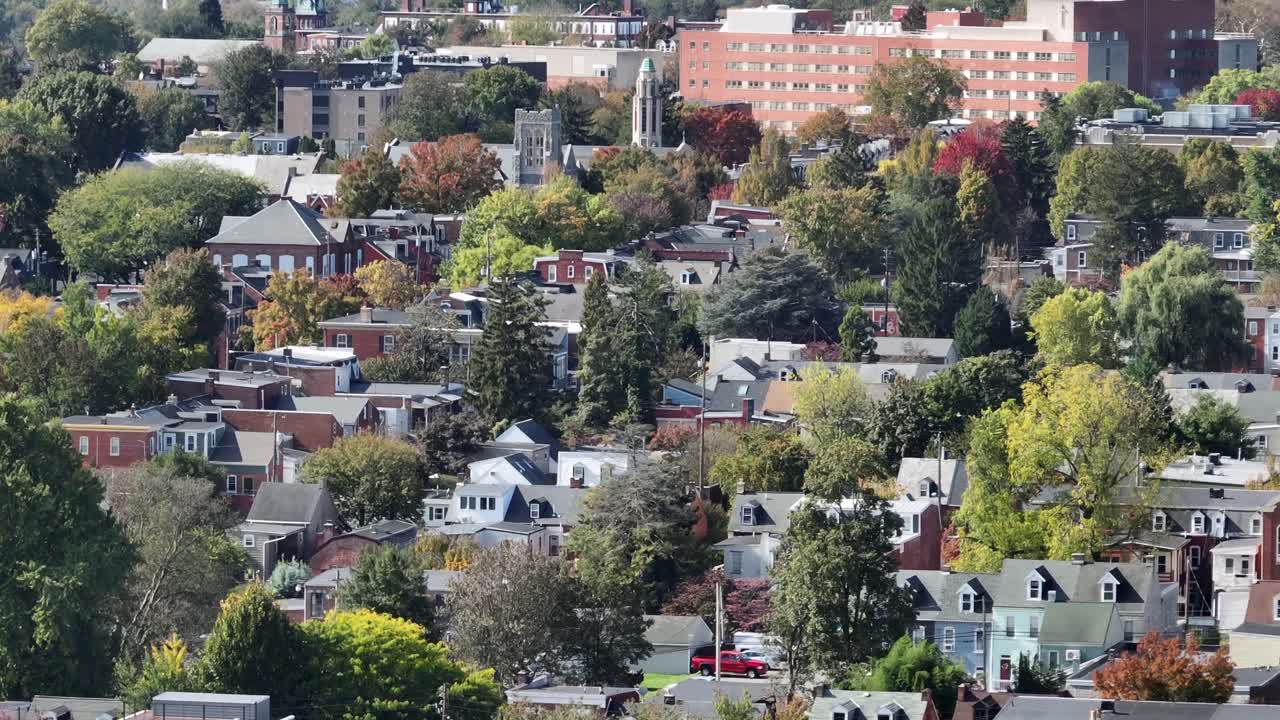 Row of houses and townhouses with downtown and church in background. Aerial wide shot. Multi colored trees In autumn season. Sunny day in historic neighborhood of america