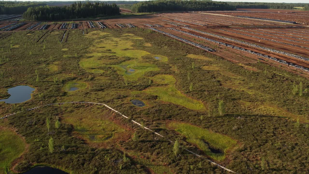 Aerial view of a large peat bog harvesting site with long parallel rows of extracted peat, wooden pallets, and covered stacks stretching across the landscape