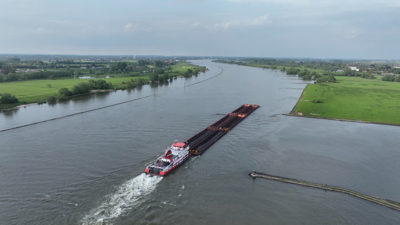 A long cargo barge navigating a wide river with green banks