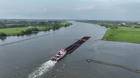 a long cargo barge navigating a wide river with green banks