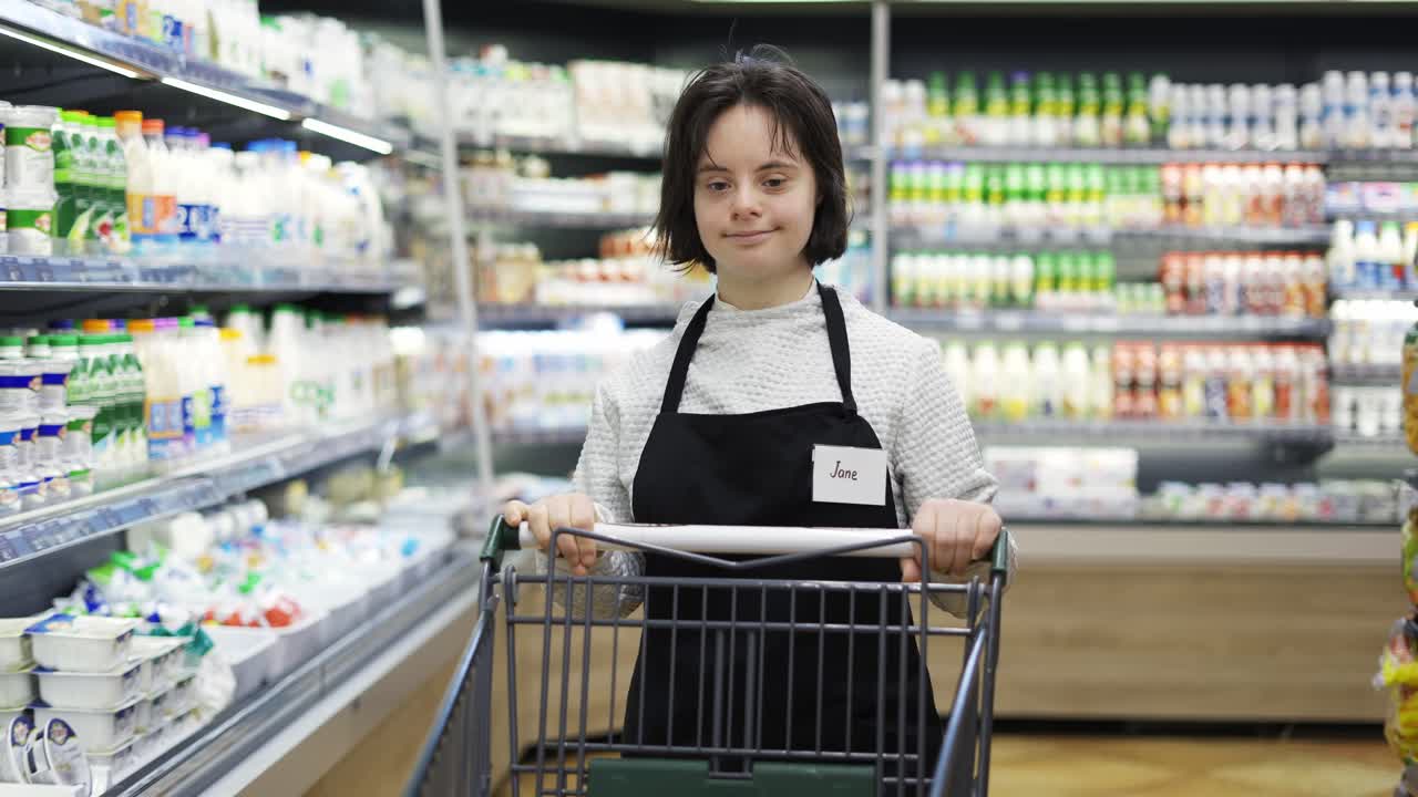 다운 증후군 을  ⁇ 고 있는 상점 직원 이 지역 슈퍼마켓 에서 쇼핑 카트를 밀고 있다