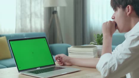 primer plano de un estudiante asiático que está somnoliento mientras mira una pantalla verde en la computadora de su casa