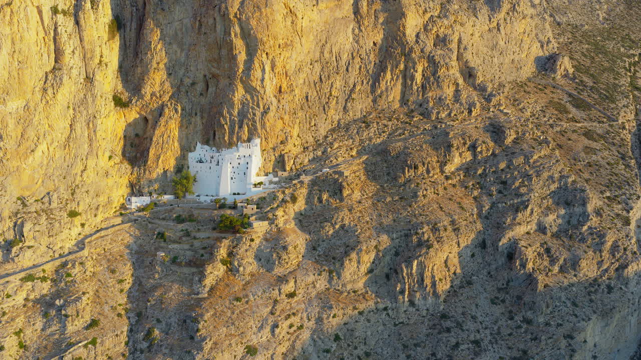 Hozoviotissa Monastery against golden cliffs at sunrise, Amorgos Island, Greece, stark contrast shadows, aerial drone orbit