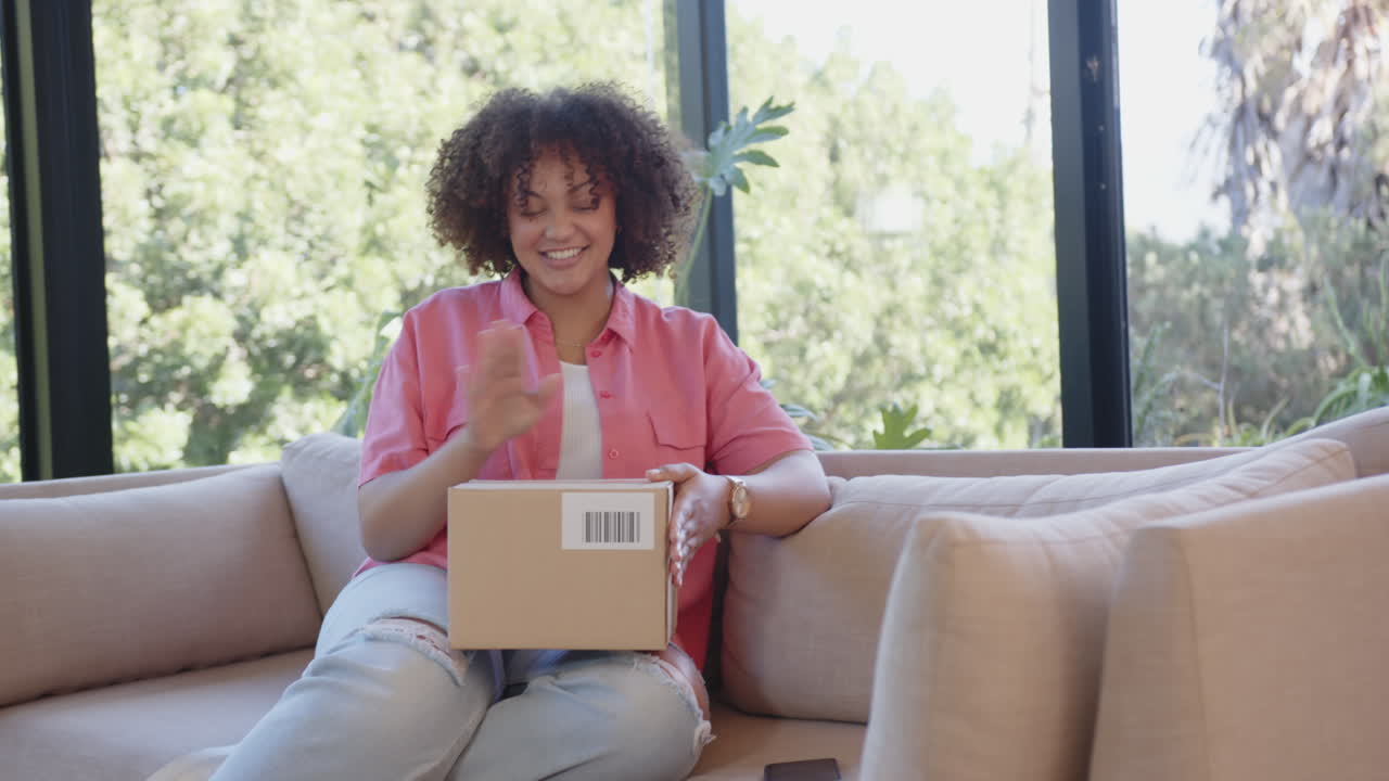 Opening package, woman sitting on couch and smiling, enjoying delivery