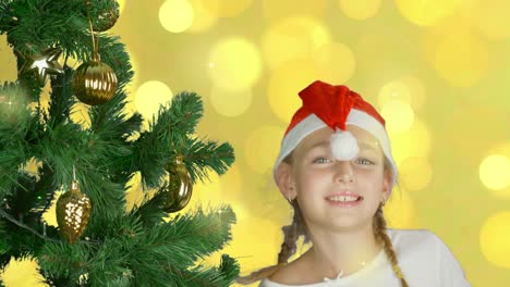 happy young girl dancing near christmas tree in santa red hat. happy young caucasian girl indoors studio close up shot. golden background. decorated christmas tree.