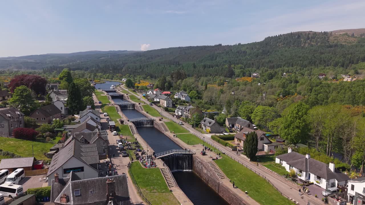 Drone view of Fort Augustus in Scotland with the Caledonian Canal crossing the village center, showing canal locks, buildings, and surrounding landscape