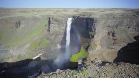 Ein-Steiler-Wasserfall,-Umgeben-Von-Felsigen-Klippen-In-Island,-Erzeugt-Einen-Kleinen-Regenbogen---Zeitlupe