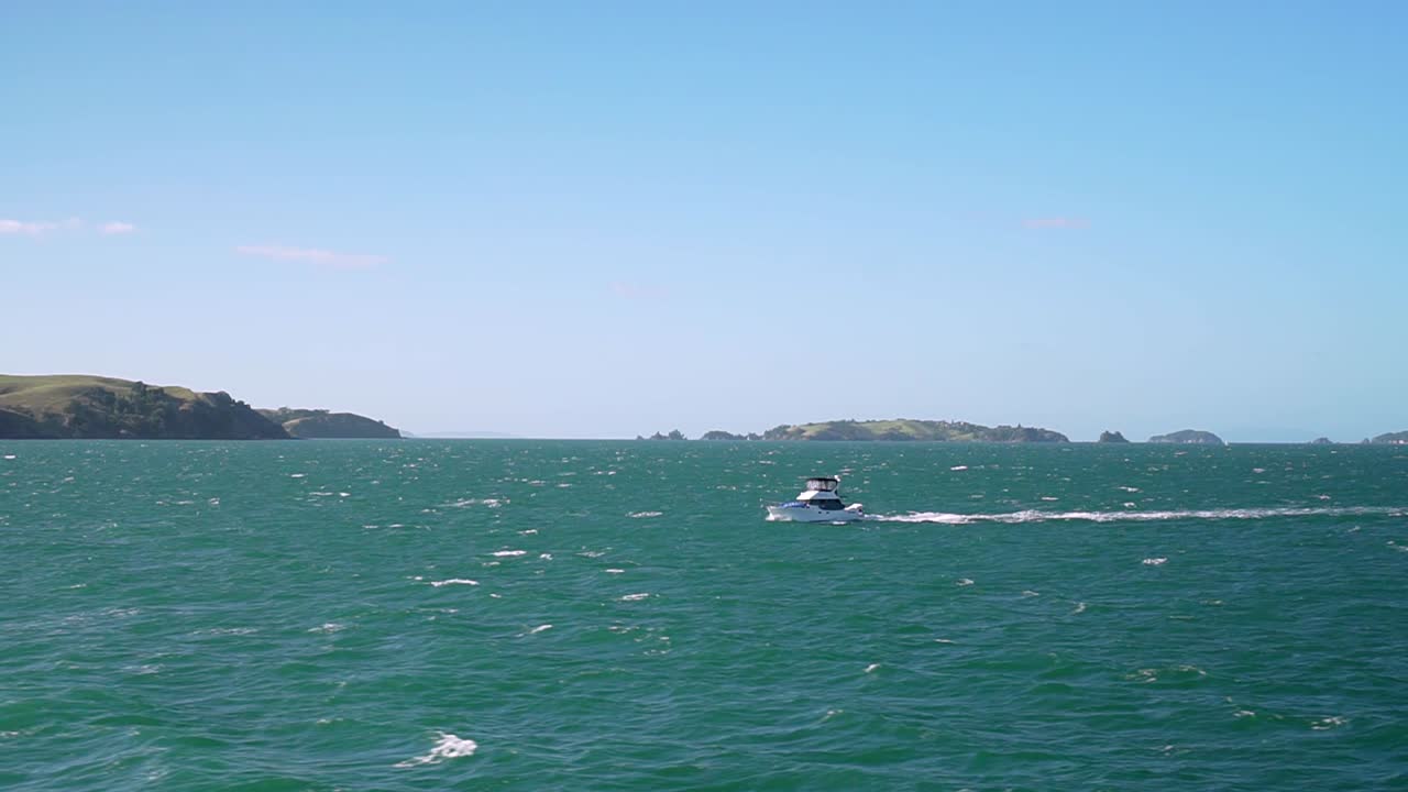 뉴질랜드, 배경에 작은 섬들이 있는 청록색 바다 위의 작은 보트의 움직이는 샷