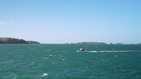 moving shot of a small boat on turquoise water ocean with small islands in background, new zealand