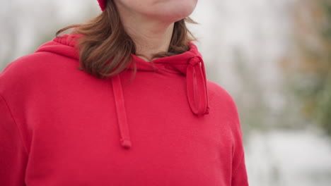 primer plano de una mujer con capucha roja en un entorno al aire libre con niebla, ajustando su correa de bolsa roja con una notable inscripción de nike en la correa, rodeada de un sereno fondo de invierno borroso con vegetación