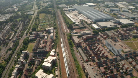 Toma-Aérea-Sobre-Trenes-Que-Pasan-Entre-La-Ciudad-Residencial-Y-El-Distrito-De-Almacenes-Basingstoke,-Reino-Unido