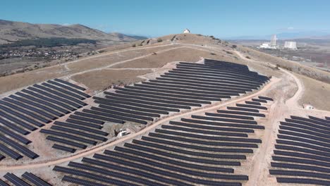 Orbit-Drohnenhügel-Mit-Photovoltaik-Solarpark-Bauernhof-Reihenpaneelen,-Altem-Kohlekraftwerk-Hintergrund