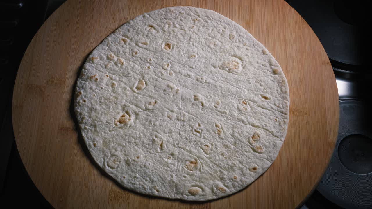 un primer plano de una envoltura de tortilla cuidadosamente cortada, los ingredientes de jamón y queso rallado se colocan estratégicamente en secciones como parte de la preparación para crear una quesadilla mexicana simple pero sabrosa