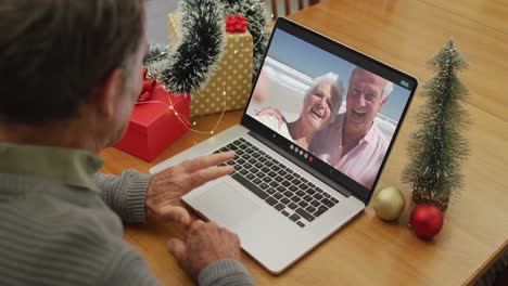 Caucasian-senior-man-on-video-call-on-laptop-with-senior-friends-at-christmas-time