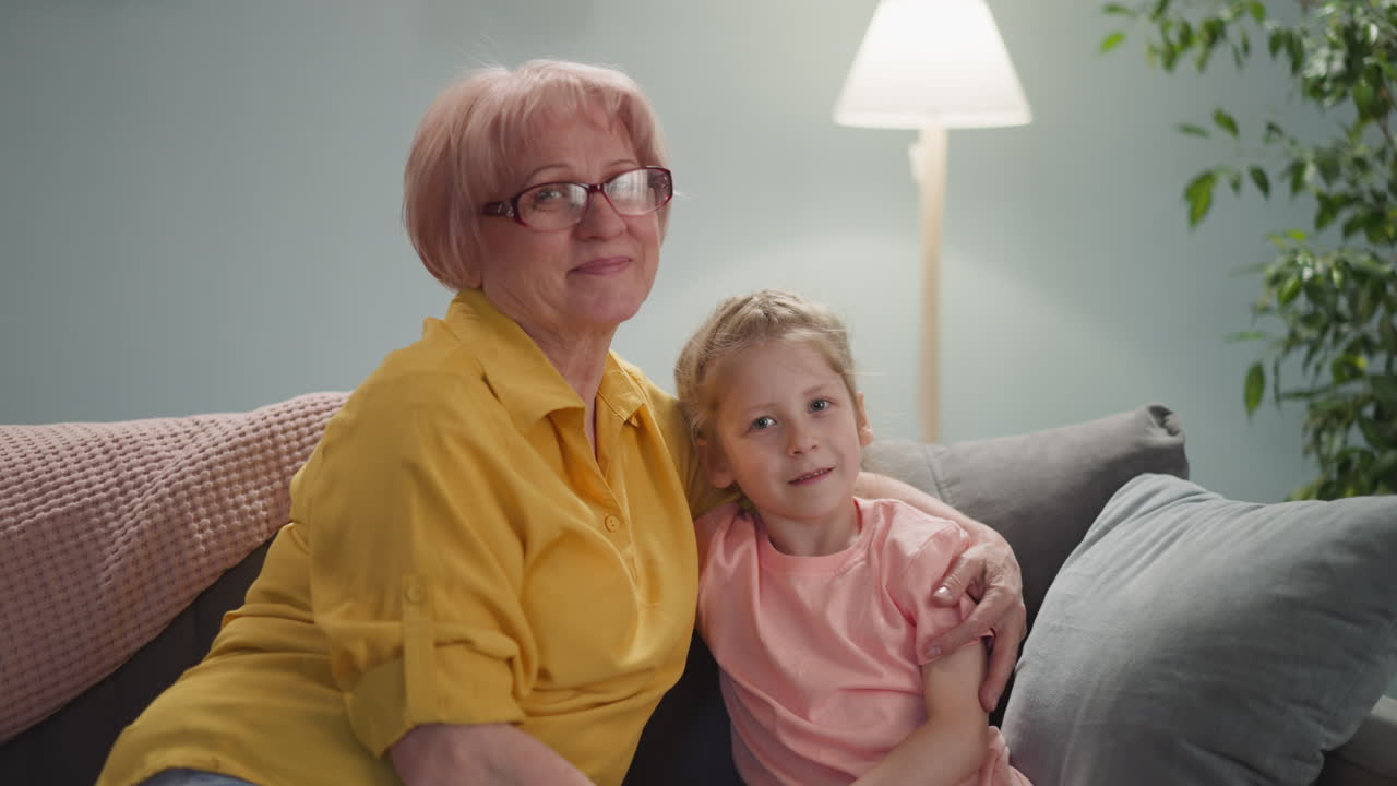 Smiling mature lady embraces granddaughter on couch posing