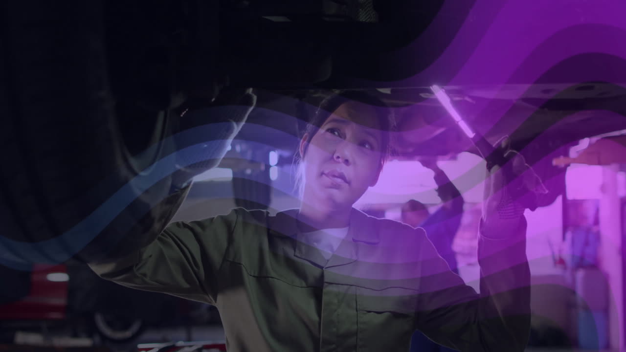 Woman mechanic shining LED light under lifted car in auto garage, with floating diagnostic icons