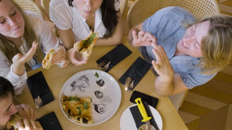 Top-View-Of-A-Group-Of-Four-Happy-Friends-Sharing-Pizza-And-Talking-At-Restaurant-1