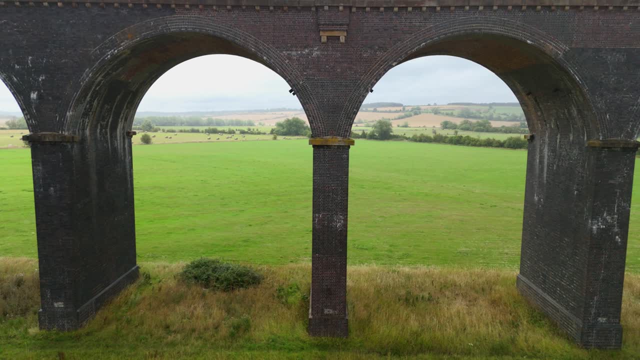 Aerial drone cinematic footage of railway viaduct with multiple arches crossing farmland and wetlands Harringworth near Corby England UK