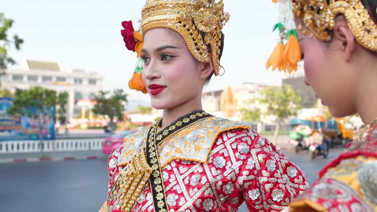 En thailandsk Khon-danser i udsmykket traditionel dragt optræder udendørs med bytrafik i baggrunden