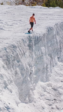 bodybuilder in the mountains. athletic man walking along the white rocky canyon. sportsman in shorts doing exercises on white hill in summer. aerial view. vertical video