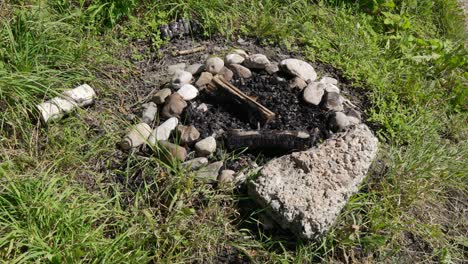 extinguished stone fireplace with burnt charred wood on a green meadow during the day in windy weather, without people