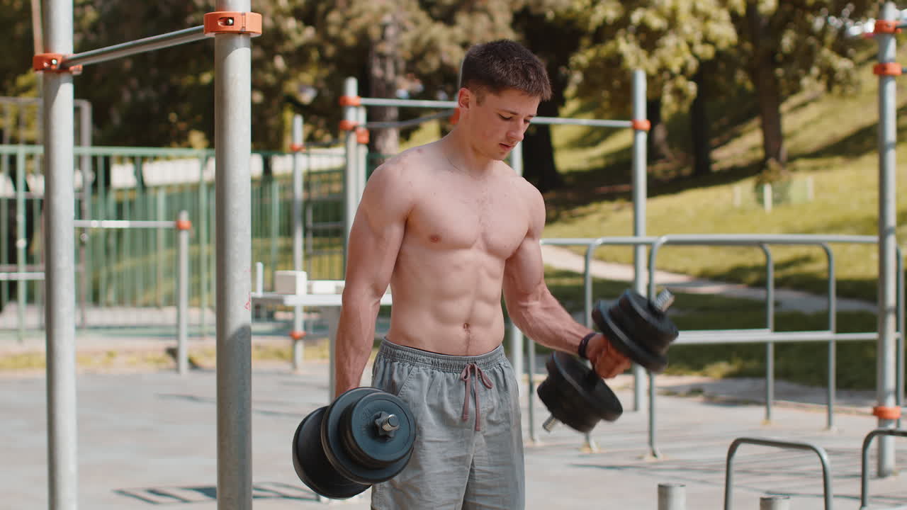 Athletic man doing arms weight lifting dumbbells exercises pumping up arm bicep muscles outdoors