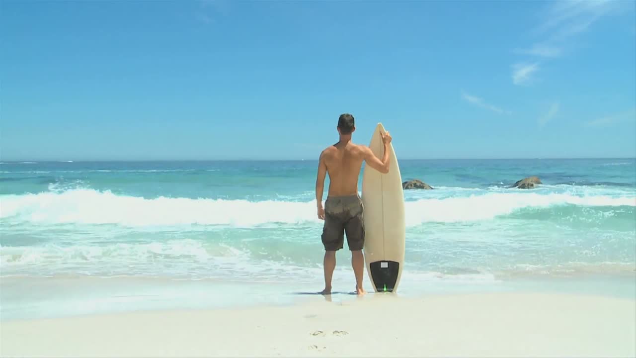 남자가 바다를 바라보고 서핑 보드를 들고 들어갑니다.