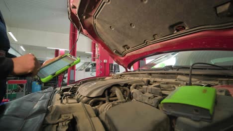 el electricista o mecánico de servicio de automóviles utiliza una tableta con software de diagnóstico interactivo futurista. inspeccionando el vehículo para encontrar componentes rotos en el compartimento del motor del automóvil moderno