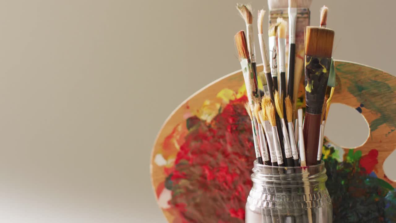 video de una colección de pinceles en un frasco y paleta utilizada en fondo gris con espacio de copia