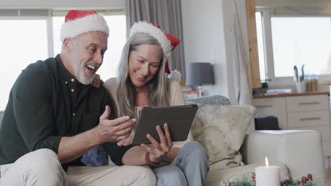 Pareja-Caucásica-De-Mediana-Edad-Con-Sombreros-De-Santa-En-Video-Chat-De-Tableta-En-Navidad-En-Casa,-Cámara-Lenta