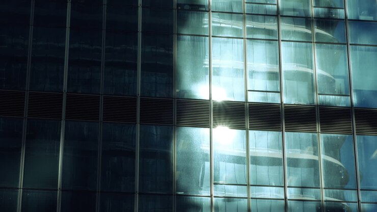 Paredes modernas de vidrio y acero con reflejos de edificios y cielo azul.