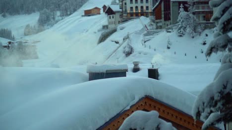 Una-Chimenea-Humeante-En-La-Azotea-Cubierta-De-Nieve-En-El-Pueblo-De-Samnaun,-Suiza