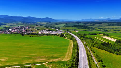 green landscape, highway, mountains. green fields stretch with a highway and mountains in the background on a sunny day