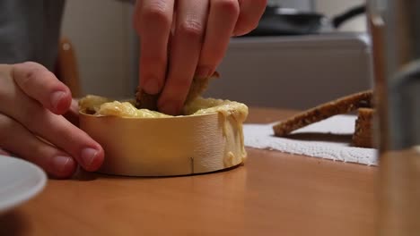 imágenes de una persona que arranca un trozo de pan y lo sumerge en una taza de queso derretido para el almuerzo o la cena
