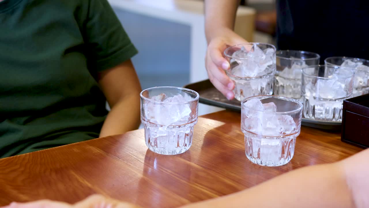 ウェイターが、着席した客のために、氷入りのグラスを木製のテーブルに並べる。