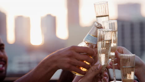 close up of friends with drinks making a toast on rooftop terrace with city skyline in background