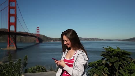 Mujer-Usando-Un-Teléfono-Inteligente-Junto-Al-Puente-Golden-Gate