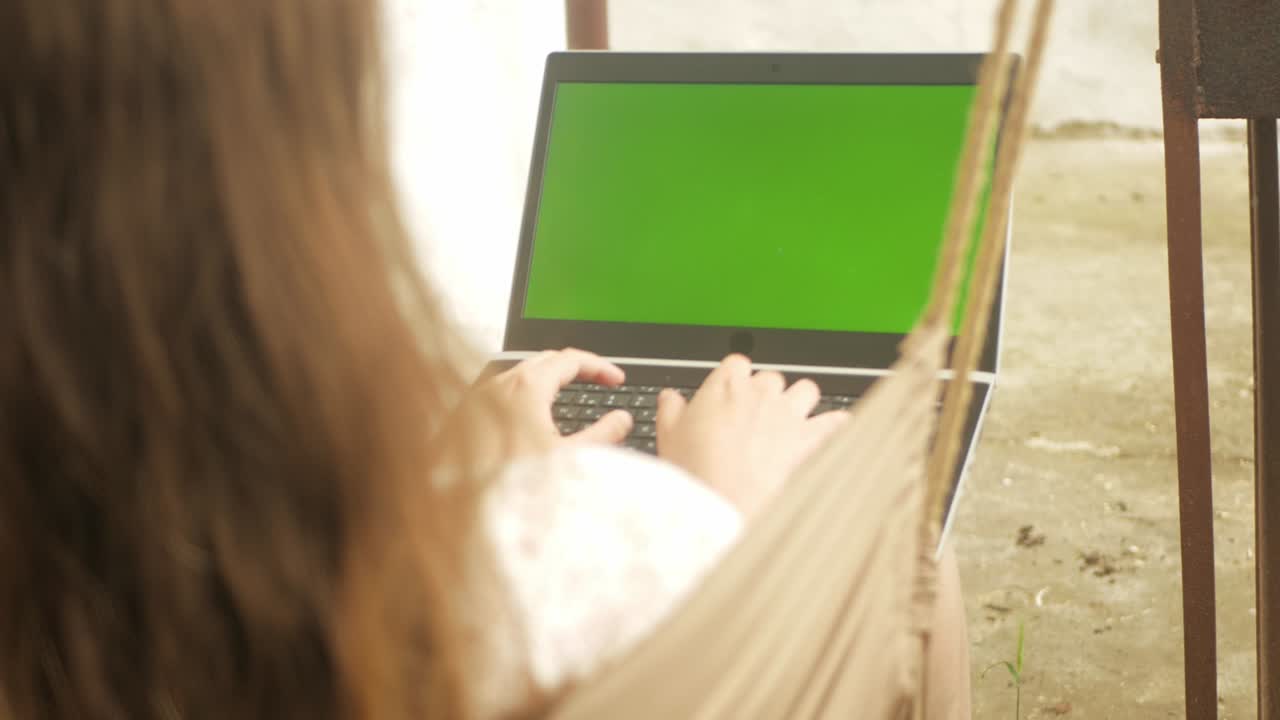 mujer monta en un columpio y se comunica con amigos usando una computadora portátil. pantalla verde, descanso en el patio de la casa. al aire libre. redes sociales, internet, mensajes. en la naturaleza. la parte de atrás del hombro
