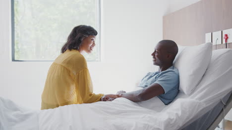 wife visiting and talking with patient husband in hospital bed