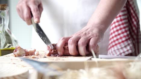 caucasian person with old hands and white apron cutting octopus tentacles and seasoning them to be cooked, on a wooden board