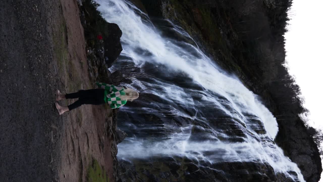 una dama rubia caminando hacia la cascada powerscourt.