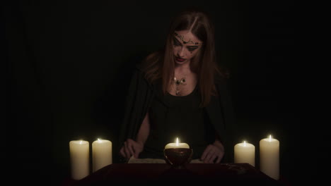 young wiccan female witch reads magic spell book to prepare for ritual in candlelight