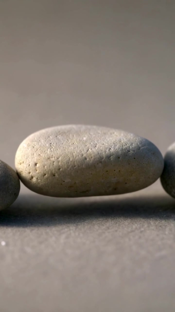 Vertical video: Shifting central oval pebble settling under gravity on sand table with side stones