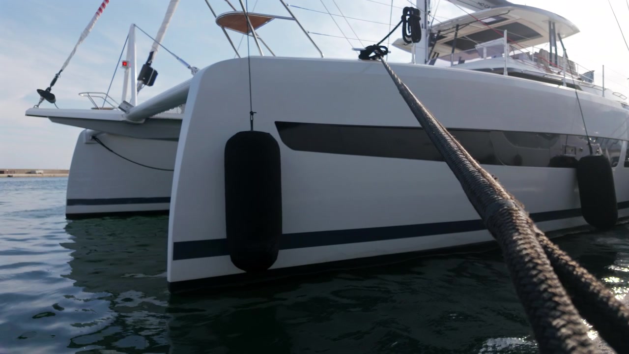 Primo piano dello scafo bianco di un catamarano con parabordi neri e una cima d'ormeggio in un molo di un porto turistico, Golfe-Juan, Francia.