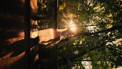 disparo vertical de una mujer espectacular en un vestido rosa posando al atardecer en un bosque