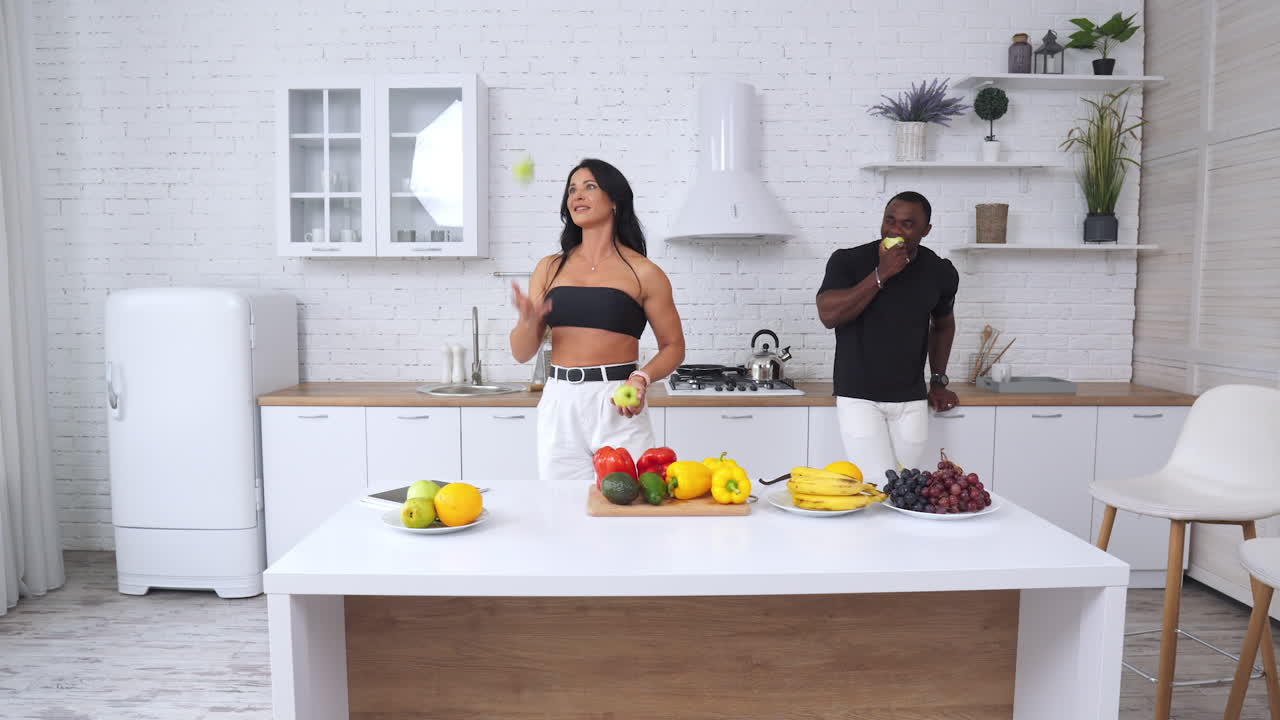 Long-haired beautiful lady trying to juggle with apples but fails. Handsome strong man watching her and laughs. Healthy food concept.